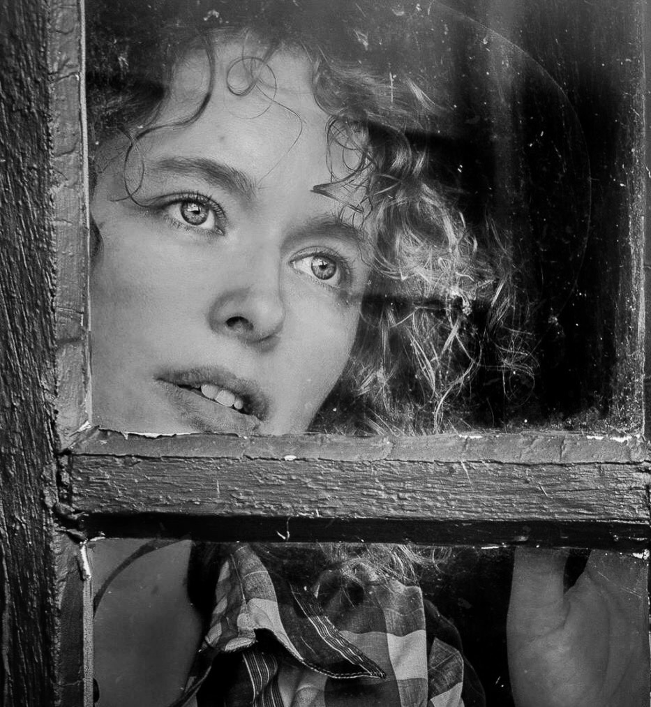 Avigail in black and white, looking out through an old window pane