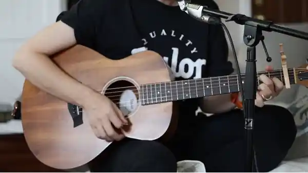 Close-up of Avigail playing an acoustic guitar with a capo, beside a microphone